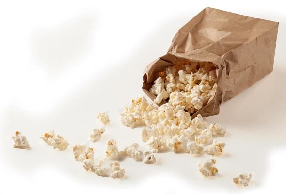 A brown paper bag with popped microwave popcorn spilling out of it.