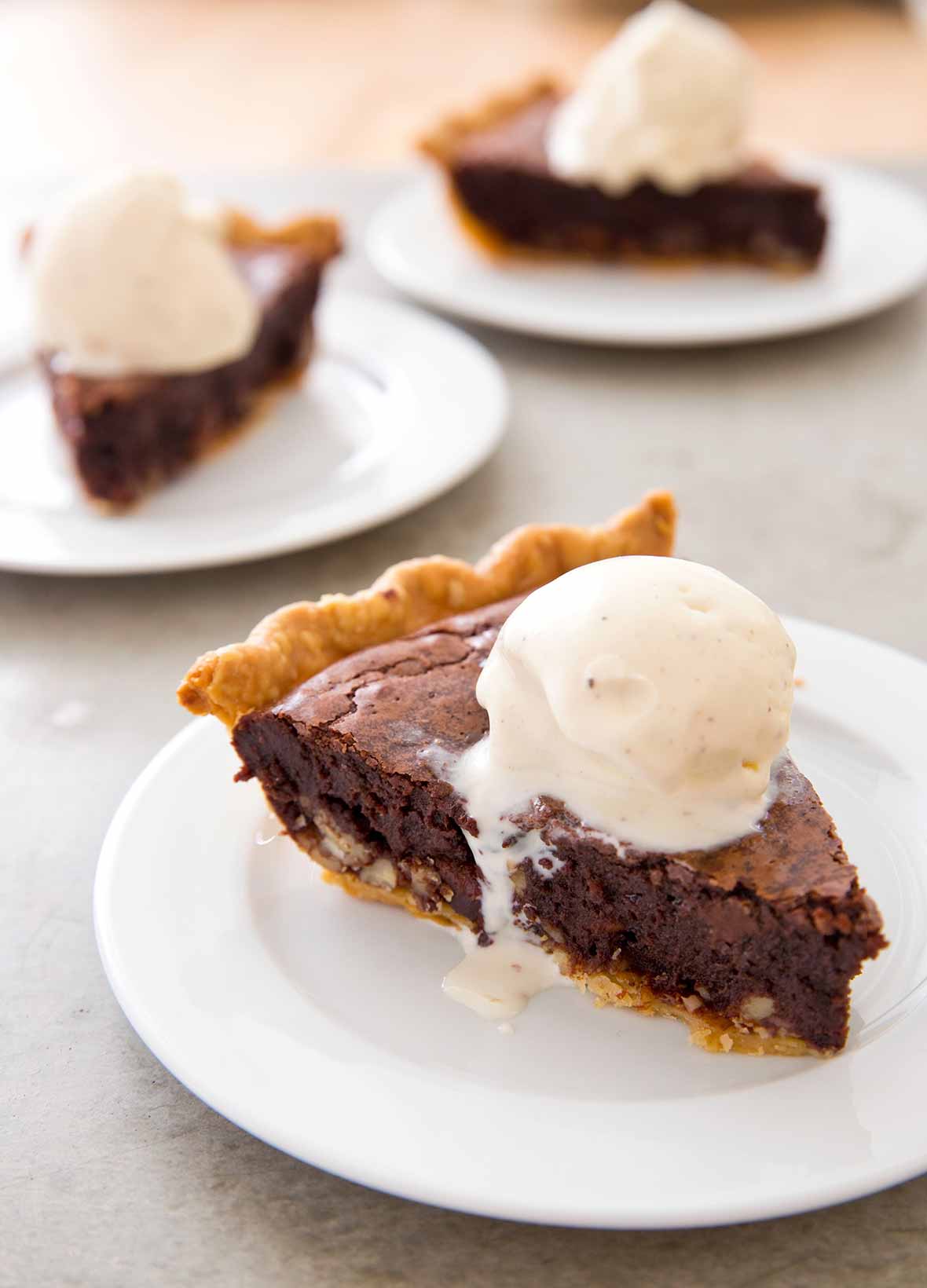 A slice of brownie tar heel pie on a white plate topped with a scoop of vanilla ice cream