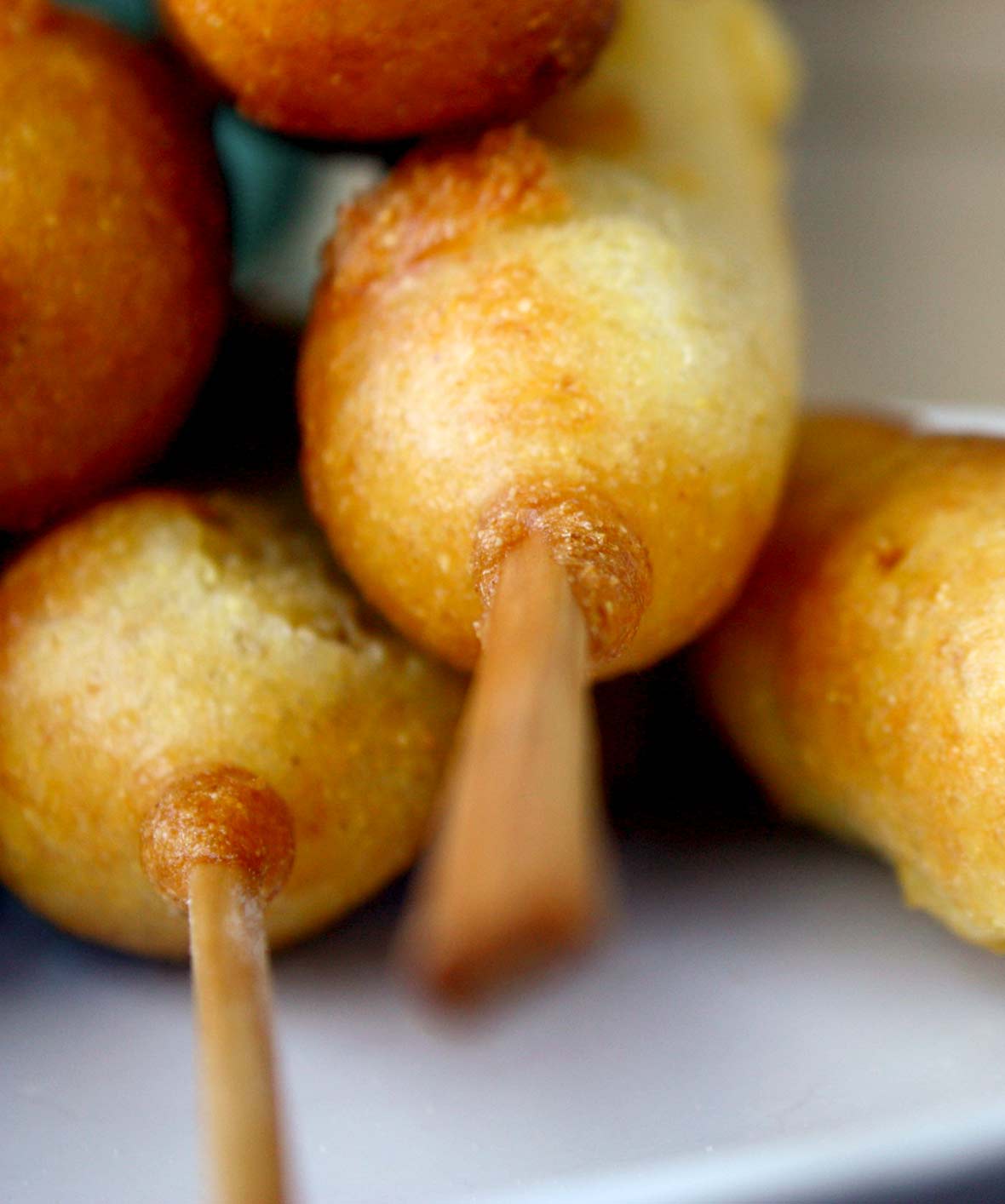 Five corn dogs with sticks on a plate