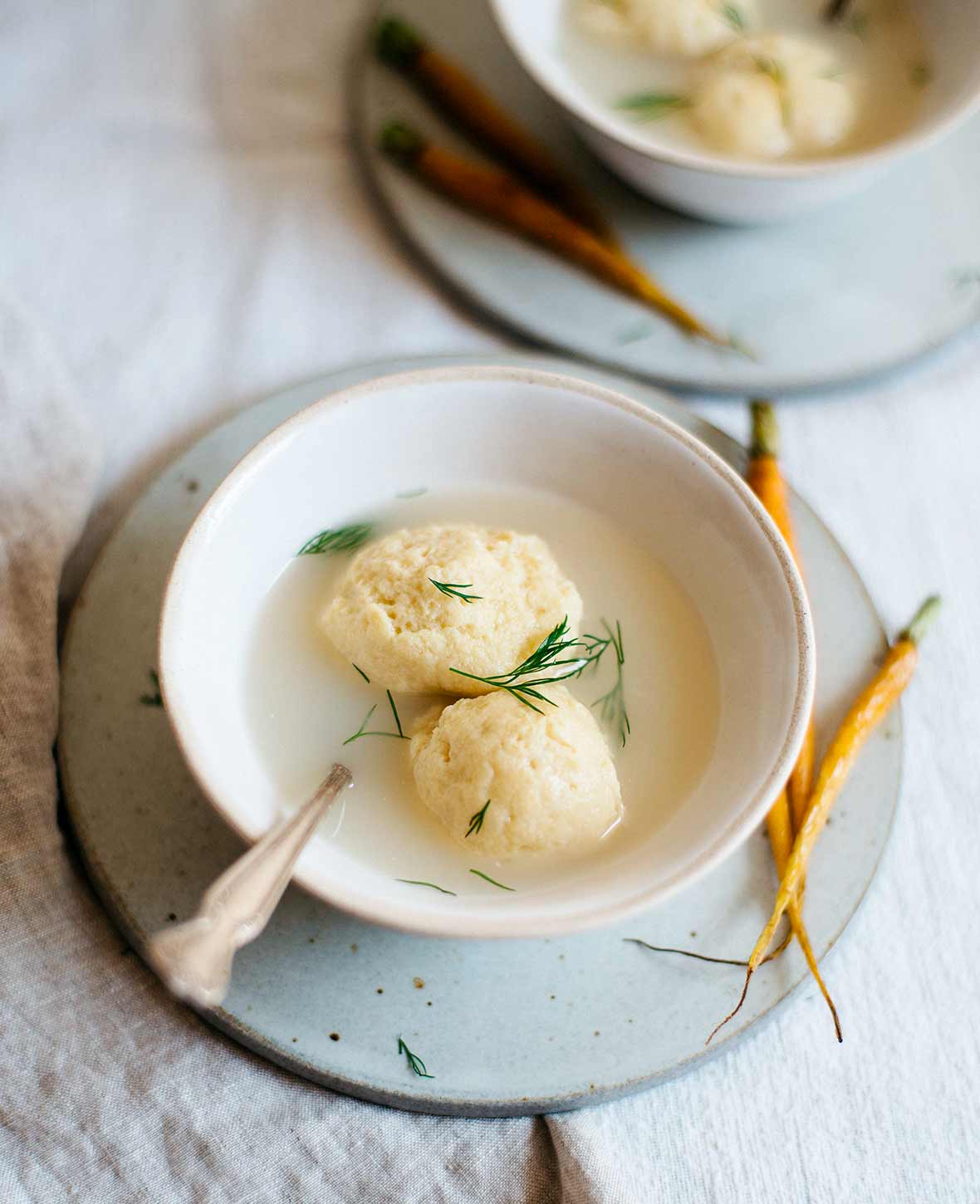 Two gluten free matzo balls in a bowl of broth garnished with dill.