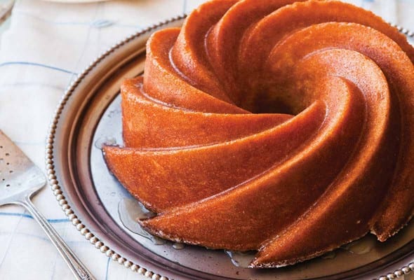 A Kentucky bourbon cake on a silver platter with a silver cake lifter and a stack of white plates beside it.