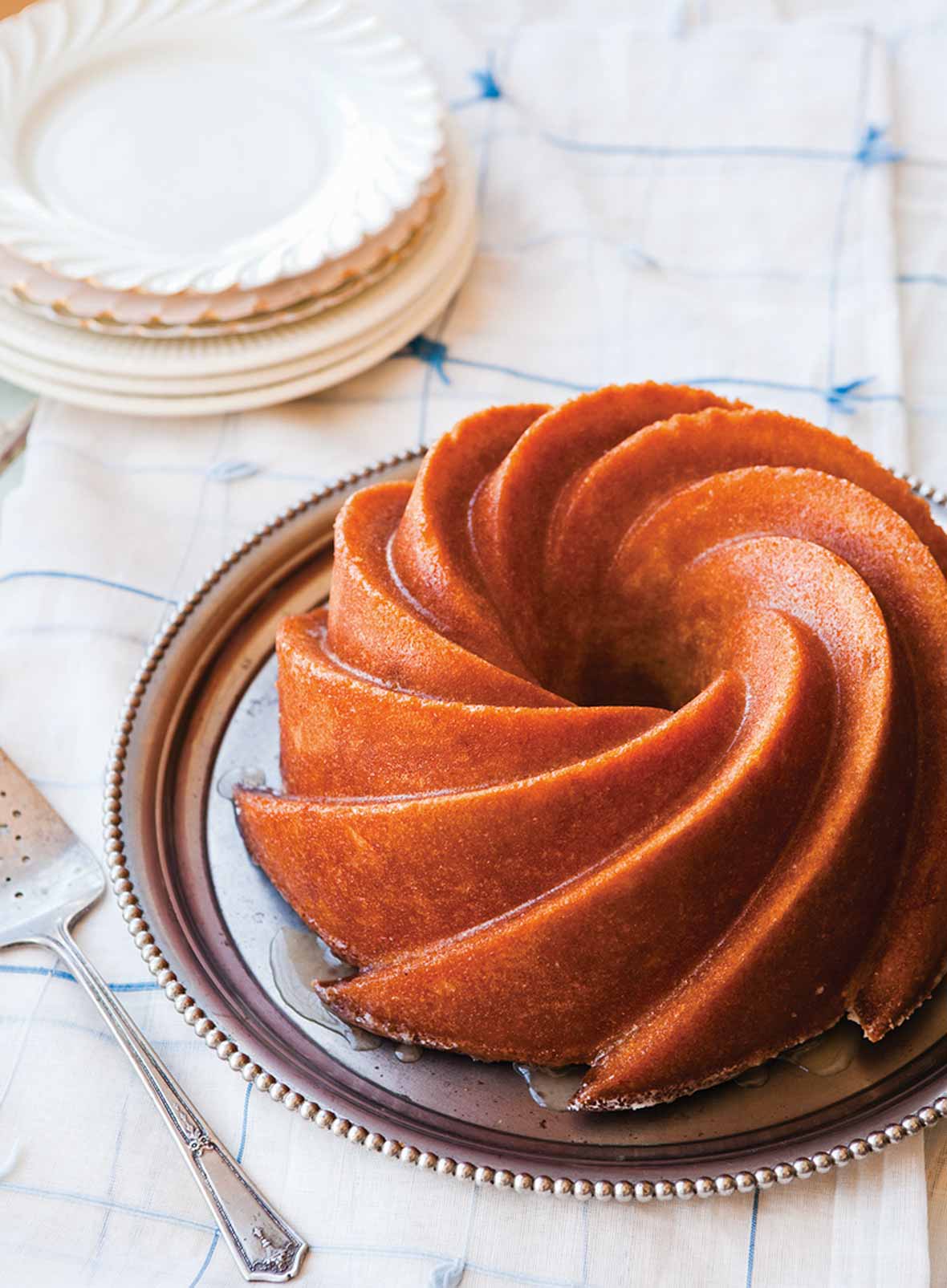 A Kentucky bourbon cake on a silver platter with a silver cake lifter and a stack of white plates beside it.