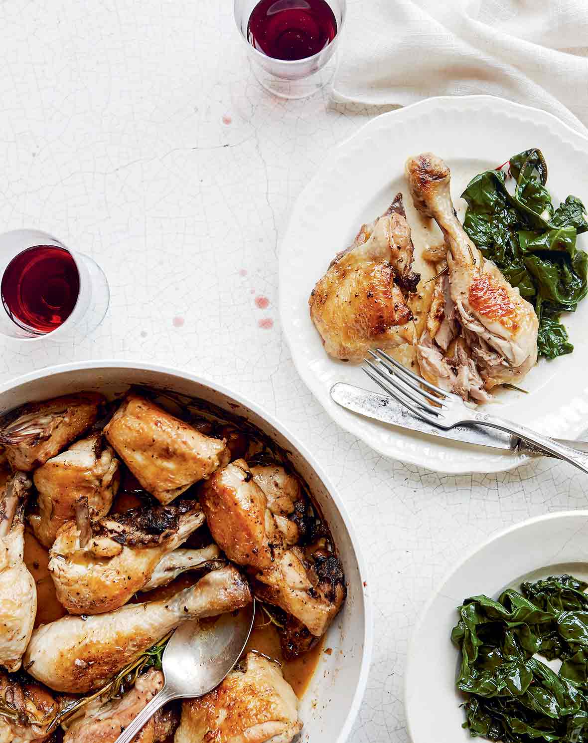 Skillet and plate with Roman chicken cacciatore--chicken pieces, rosemary, and garlic on white wood