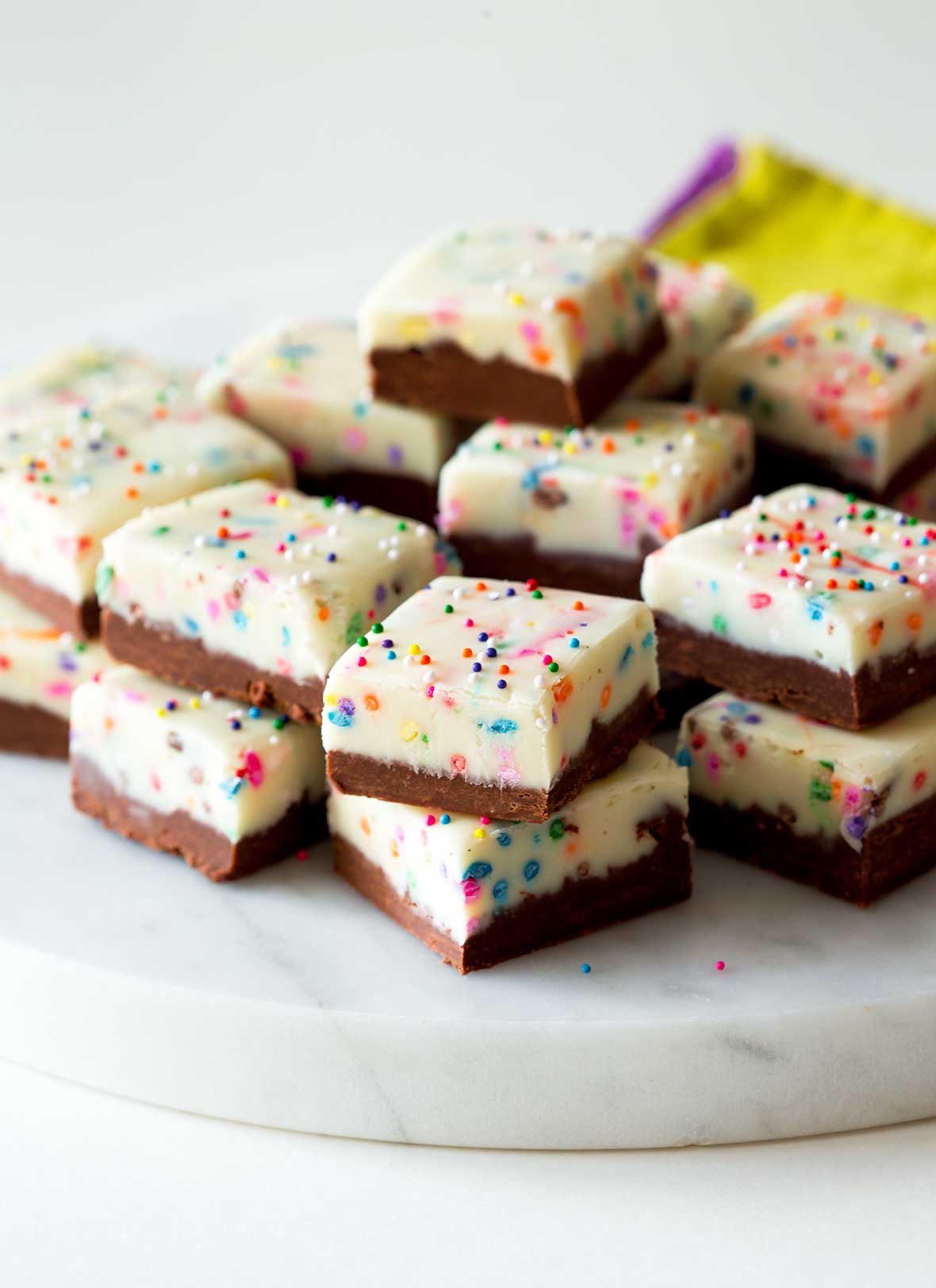 A stack of squares of birthday cake fudge on a white marble platter.
