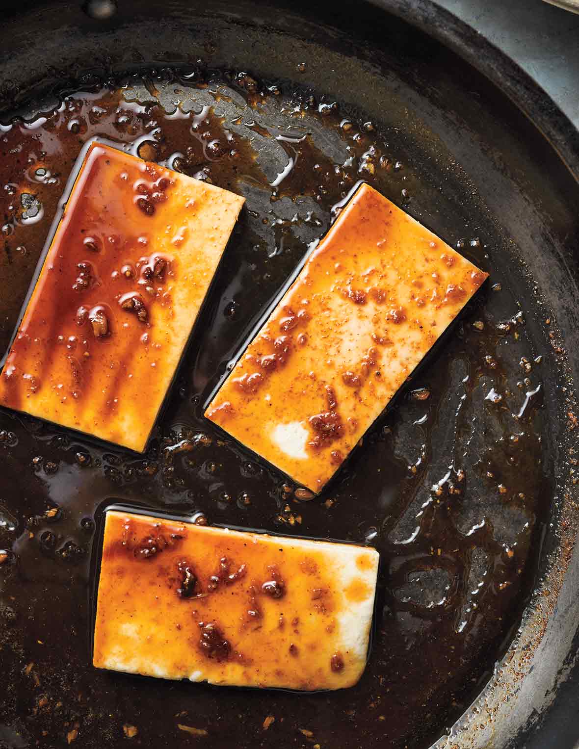 Three portions of glazed tofu in a skillet