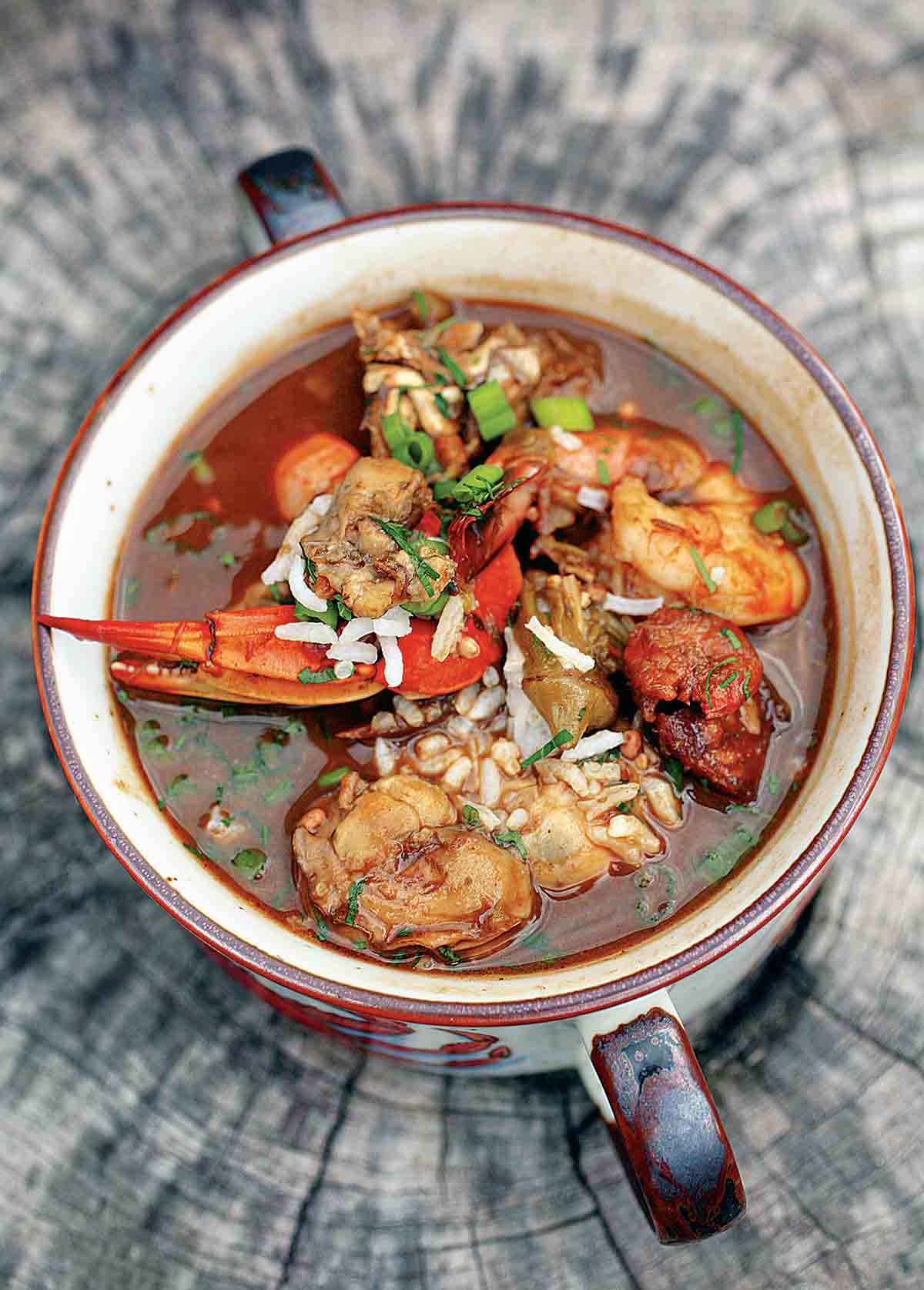 A two-handle bowl of seafood gumbo on a piece of wood.