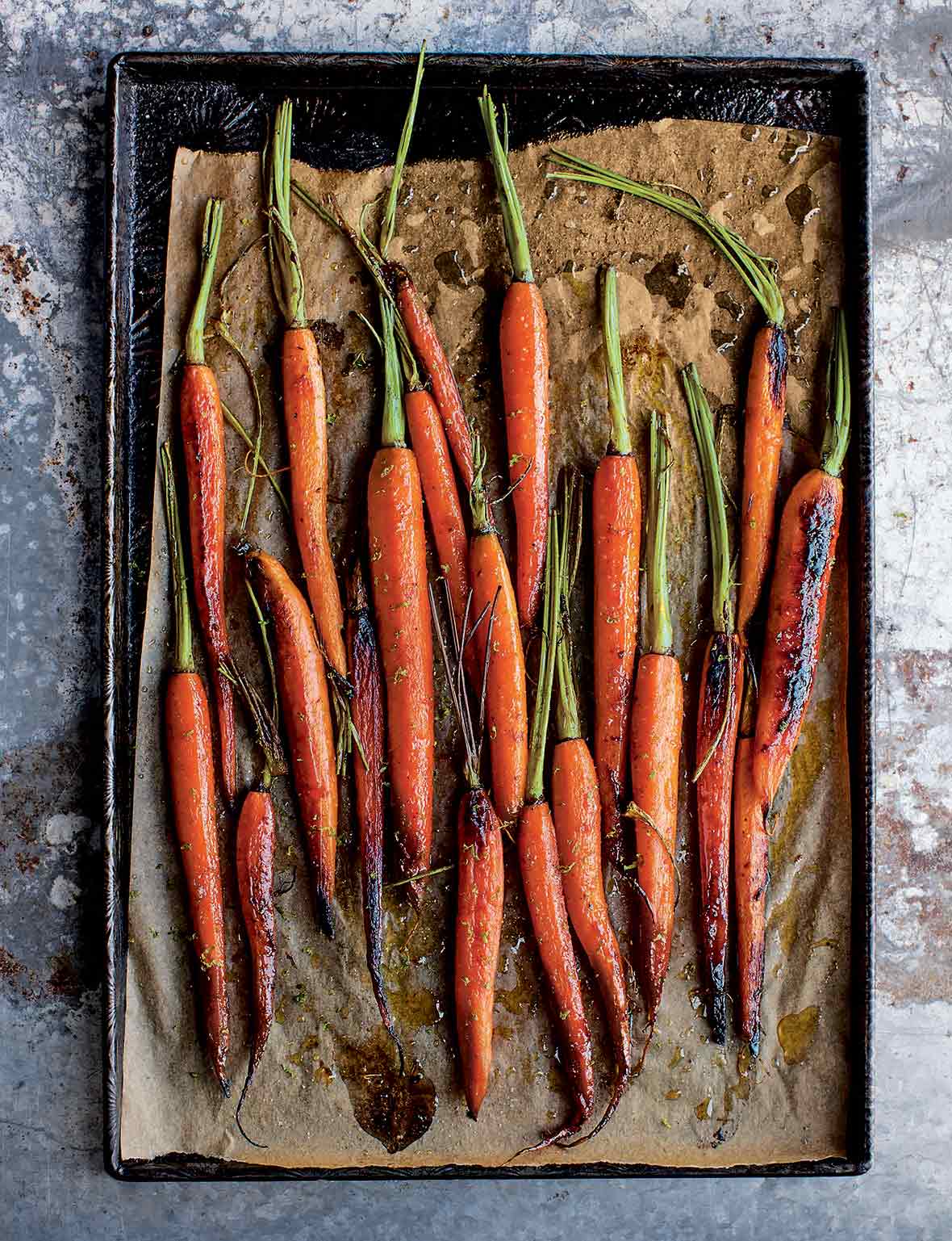 A bunch of roasted sweet and spicy carrots on a parchment-lined baking sheet.