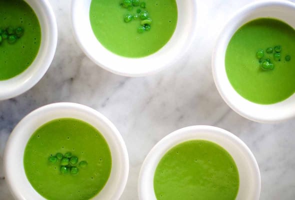 Five white bowls filled with pureed cold sweet pea soup, topped with a few who peas