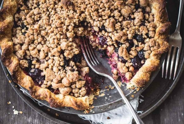 A bluebarb pie with one slice missing and two forks resting beside the pie.