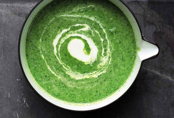A saucepan filled with green soup, with a swirl of cashew cream in the center.