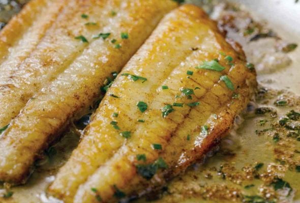 Two fillets of flounder in a lemon butter sauce in a skillet topped with chopped parsley