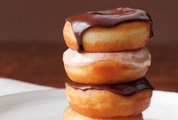 Four glazed doughnuts stacked on top of each other, two with chocolate glaze, 2 with vanilla glaze