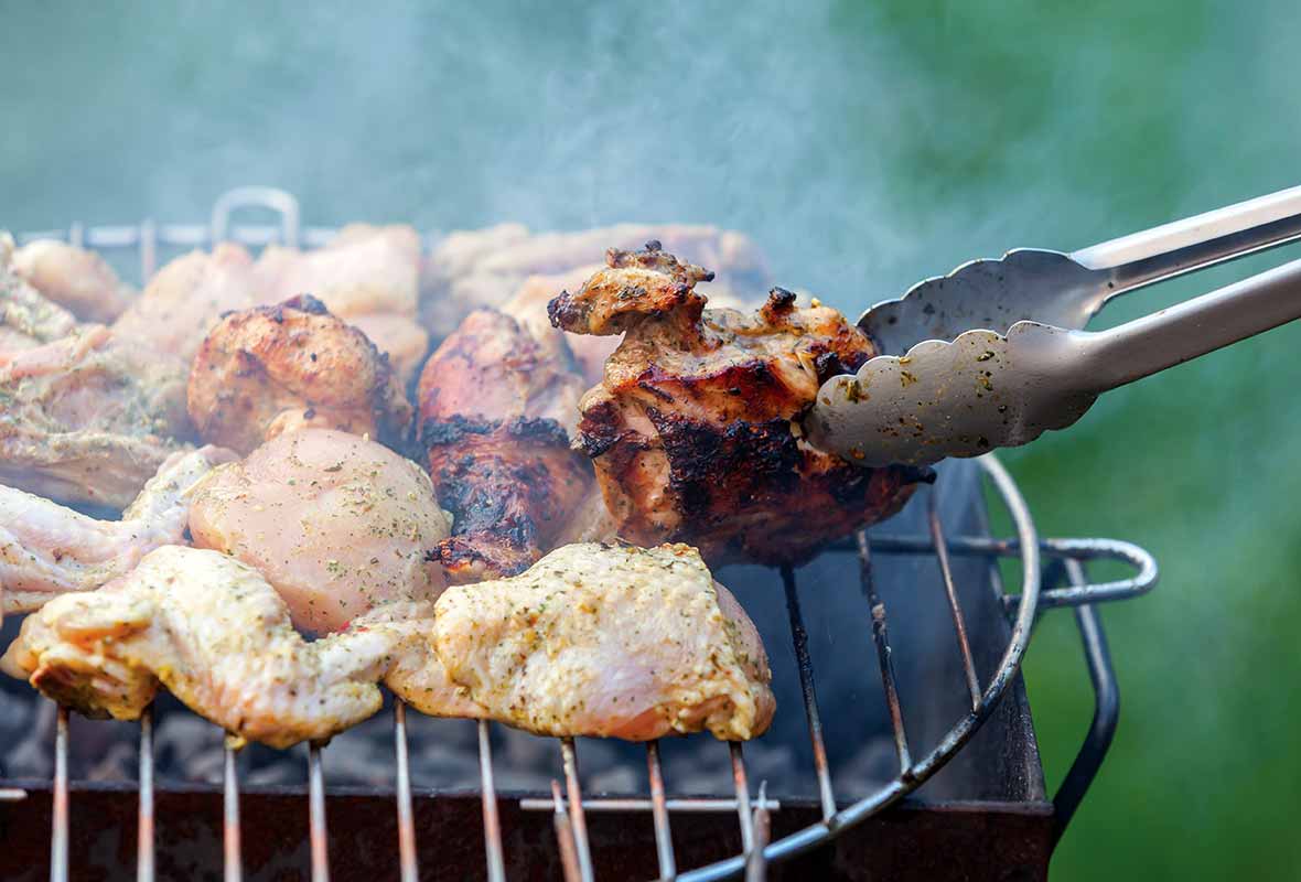 Pieces of grilled chicken with balsamic vinaigrette cooking on a grill, being turned with a pair of tongs.