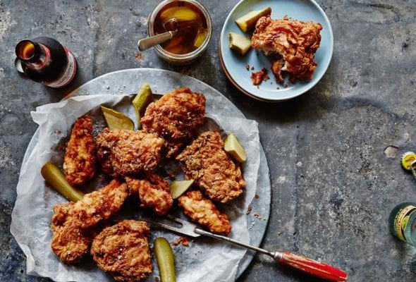 A platter of pickle-brined fried chicken with pieces of dill pickle, and a bottle of beer.