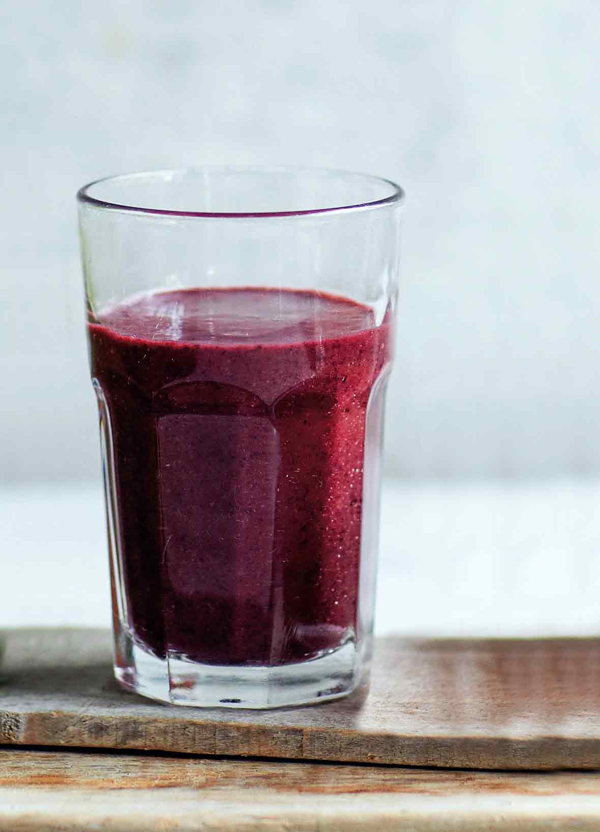 A glass of blueberry spinach smoothie on a wooden plank.