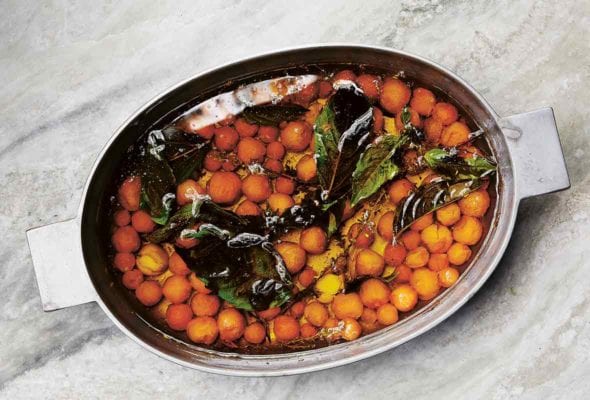 A Dutch oven filled with a cherry tomato confit of Sun Gold cherry tomatoes, oil, and fresh basil leaves.