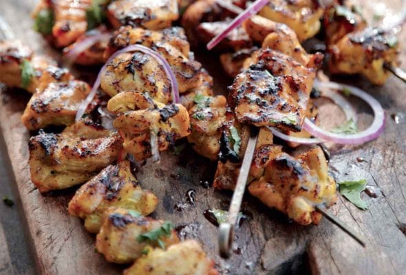 Seven grilled chicken skewers with red onion, coconut milk, and cilantro on a wooden board