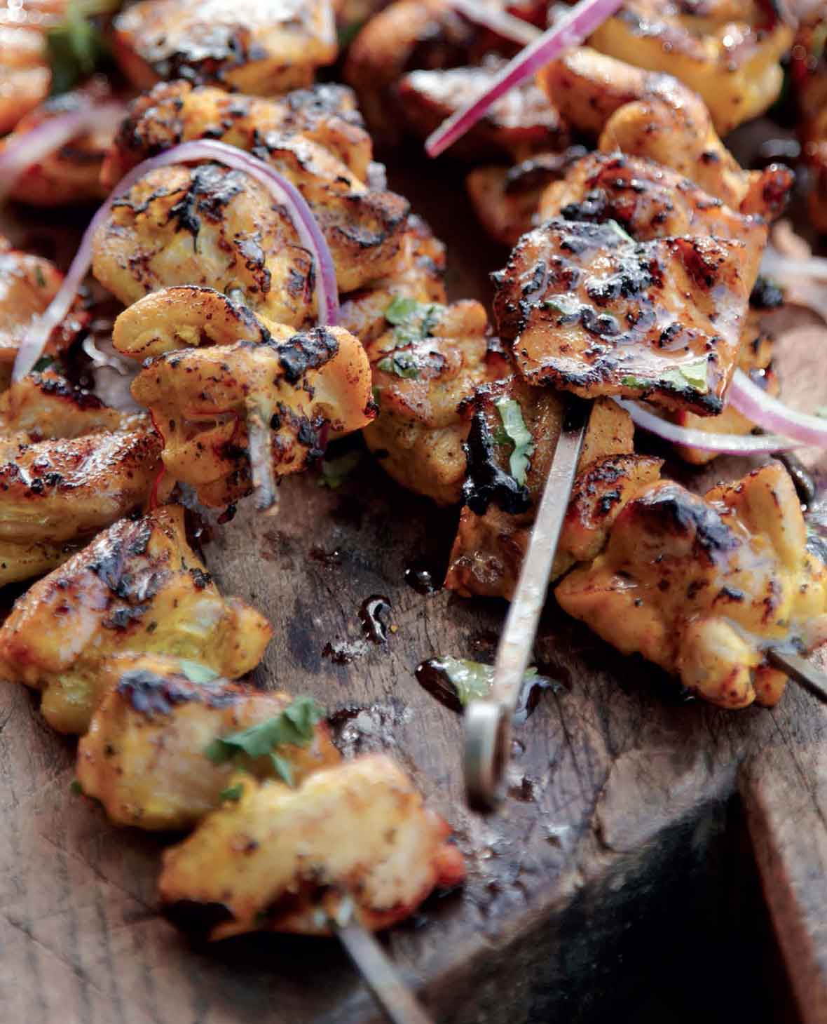 Seven grilled chicken skewers with red onion, coconut milk, and cilantro on a wooden board