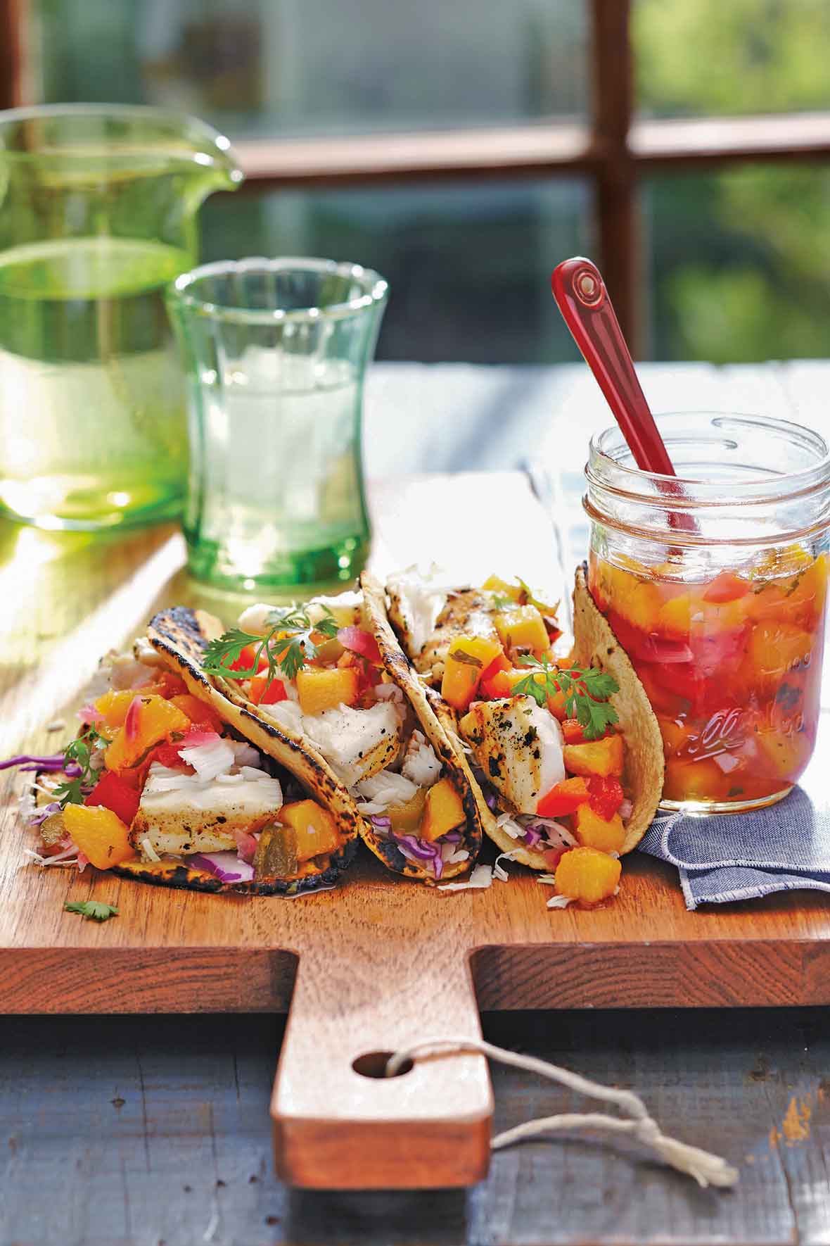 An open jar of peach salsa next to three fish tacos topped with peach salsa.
