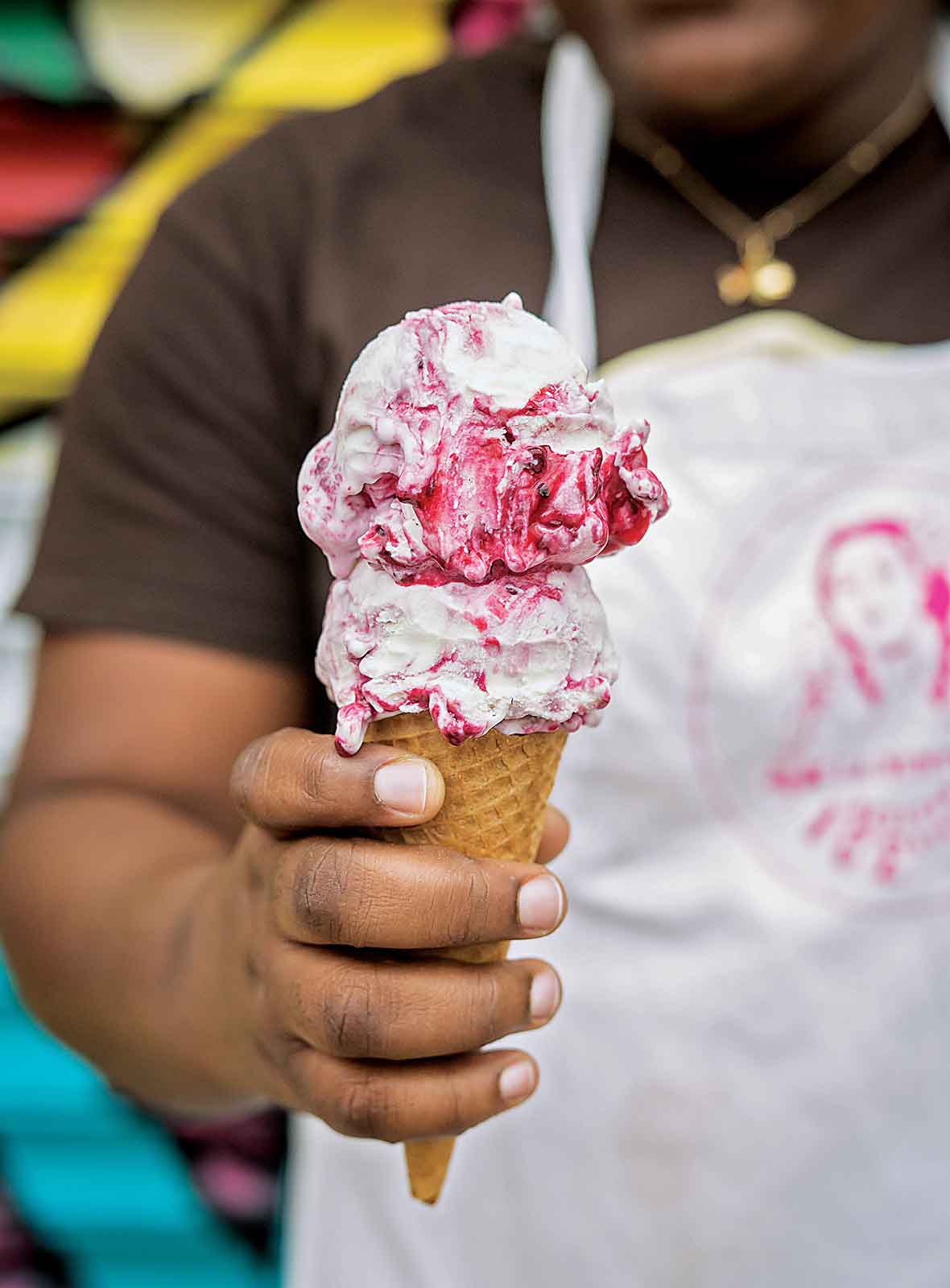 A person holding a sugar cone topped with two scoops of blackberry ice cream.