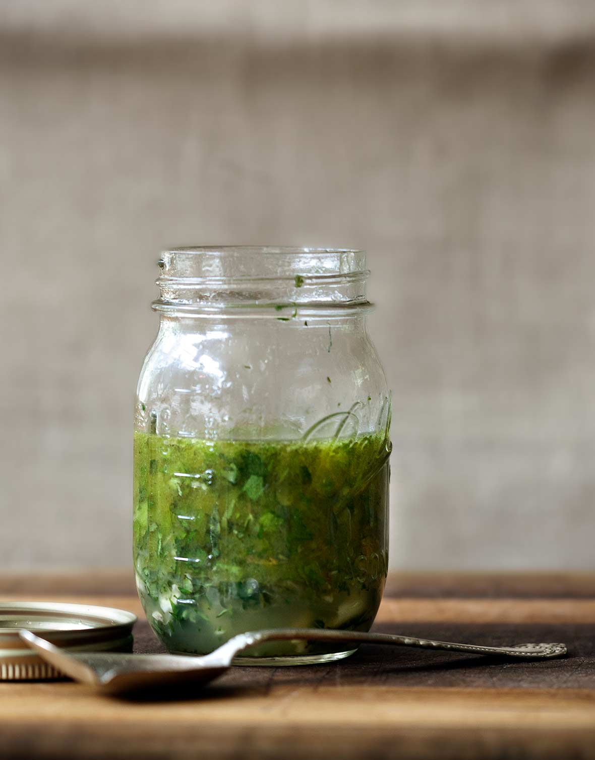 Mason jar of Greek marinade with parsley, oregano, thyme, rosemary, basil on a cutting board