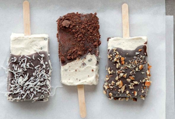 Three homemade ice cream bars, coated with chocolate and sprinkled with almonds, coconut, and chocolate crumbs.