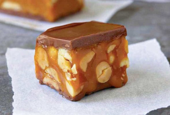 A square piece of homemade snickers bar on a piece of parchment.