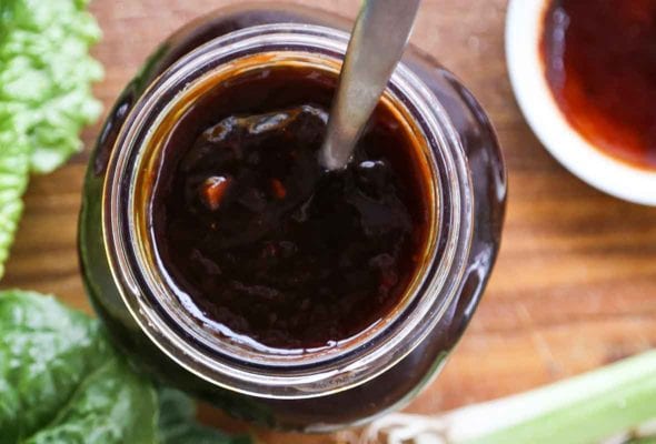 A glass jar filled with Korean barbecue sauce, with some greens beside it.