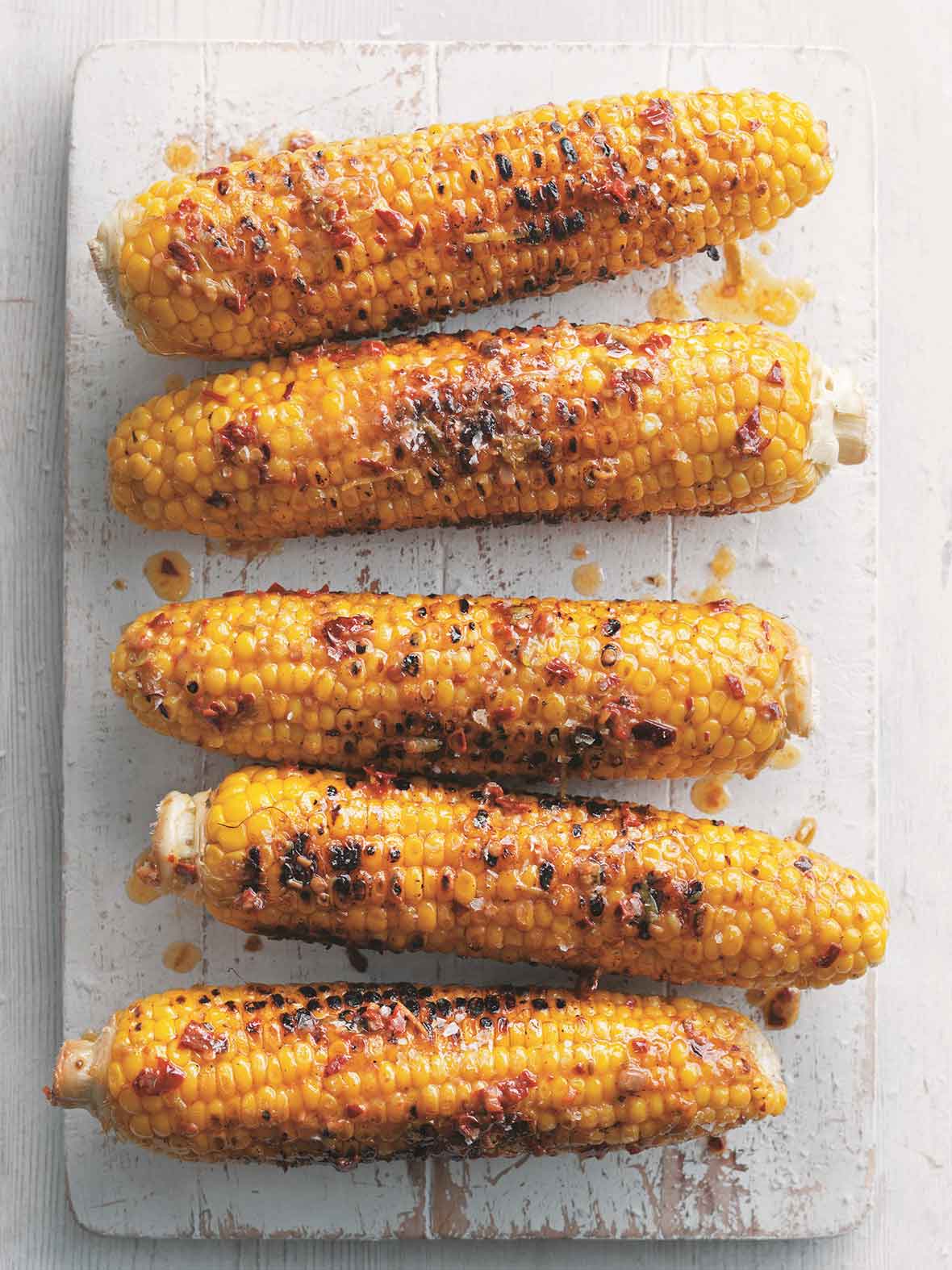 Five ears of Mexican corn on the cob on a white wooden board.