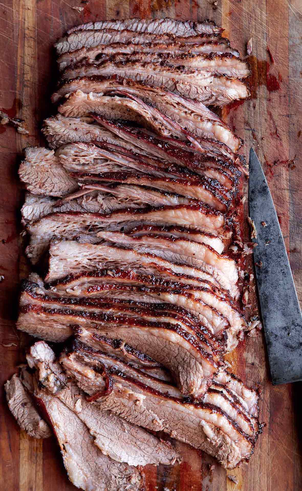 A sliced Texas brisket on a wooden board with a knife lying beside it.