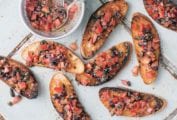 Eight slices of tomato bruschetta with a bowl of bruschetta topping on the side.