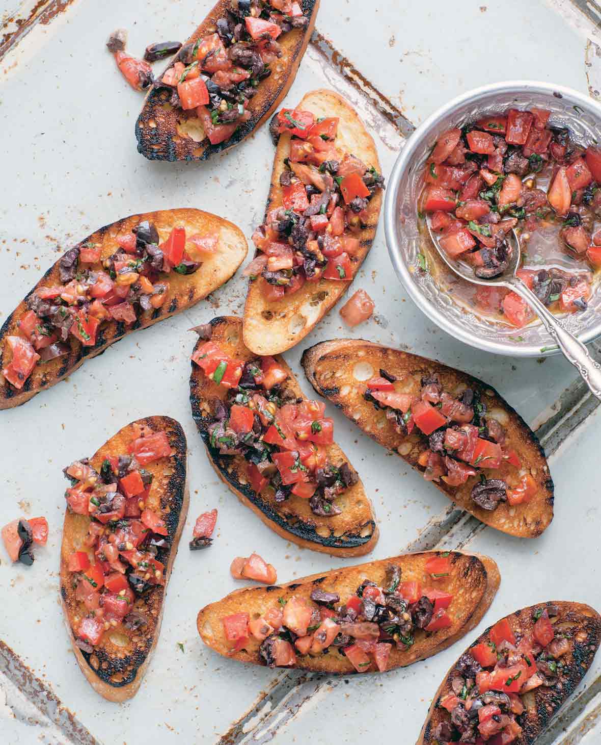 Eight slices of tomato bruschetta with a bowl of bruschetta topping on the side.