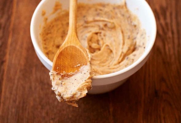 A white bowl partially filled with cookie dough buttercream frosting with a wooden spoon resting on top.