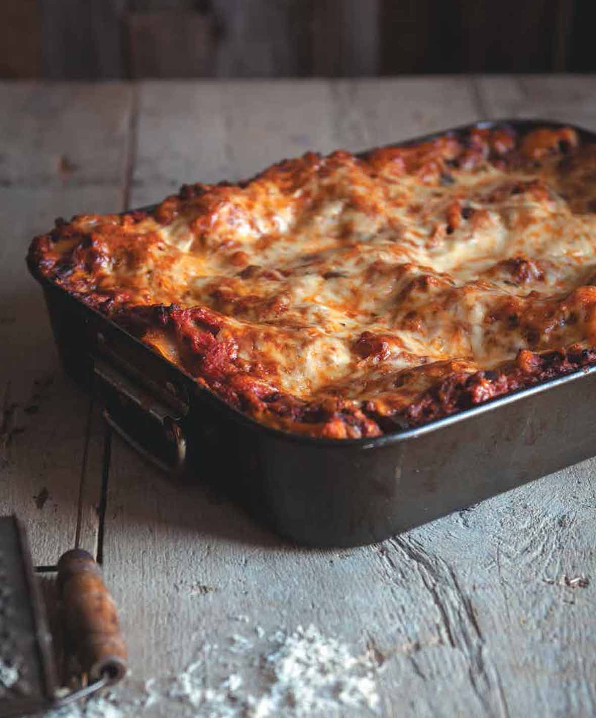 A metal baking dish filled with lasagna bolognese on a wooden surface.