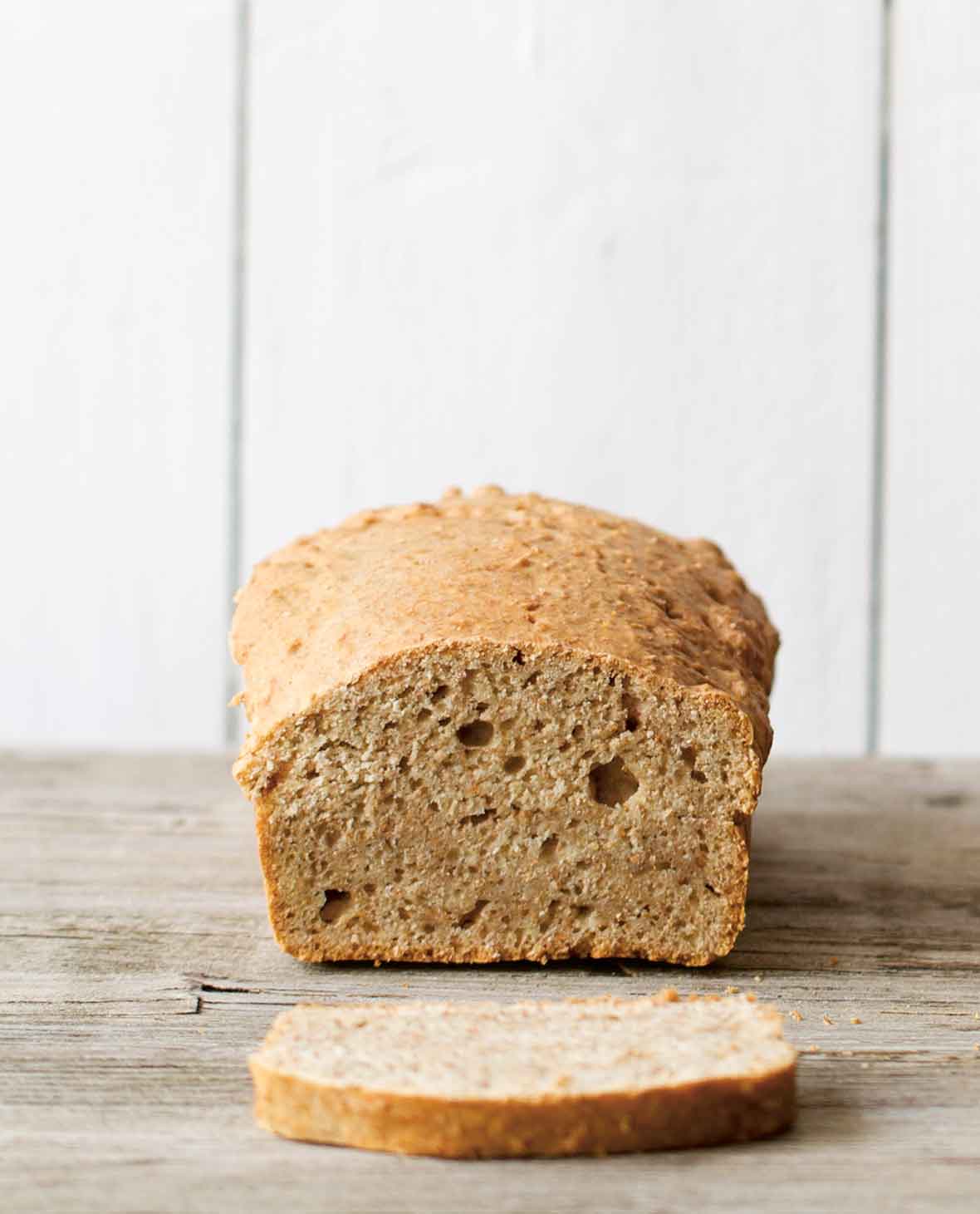 A loaf of beer bread with a slice cut off on a wooden surface.