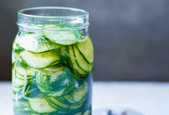 An open jar of refrigerator sweet pickles with the lid lying beside the jar.