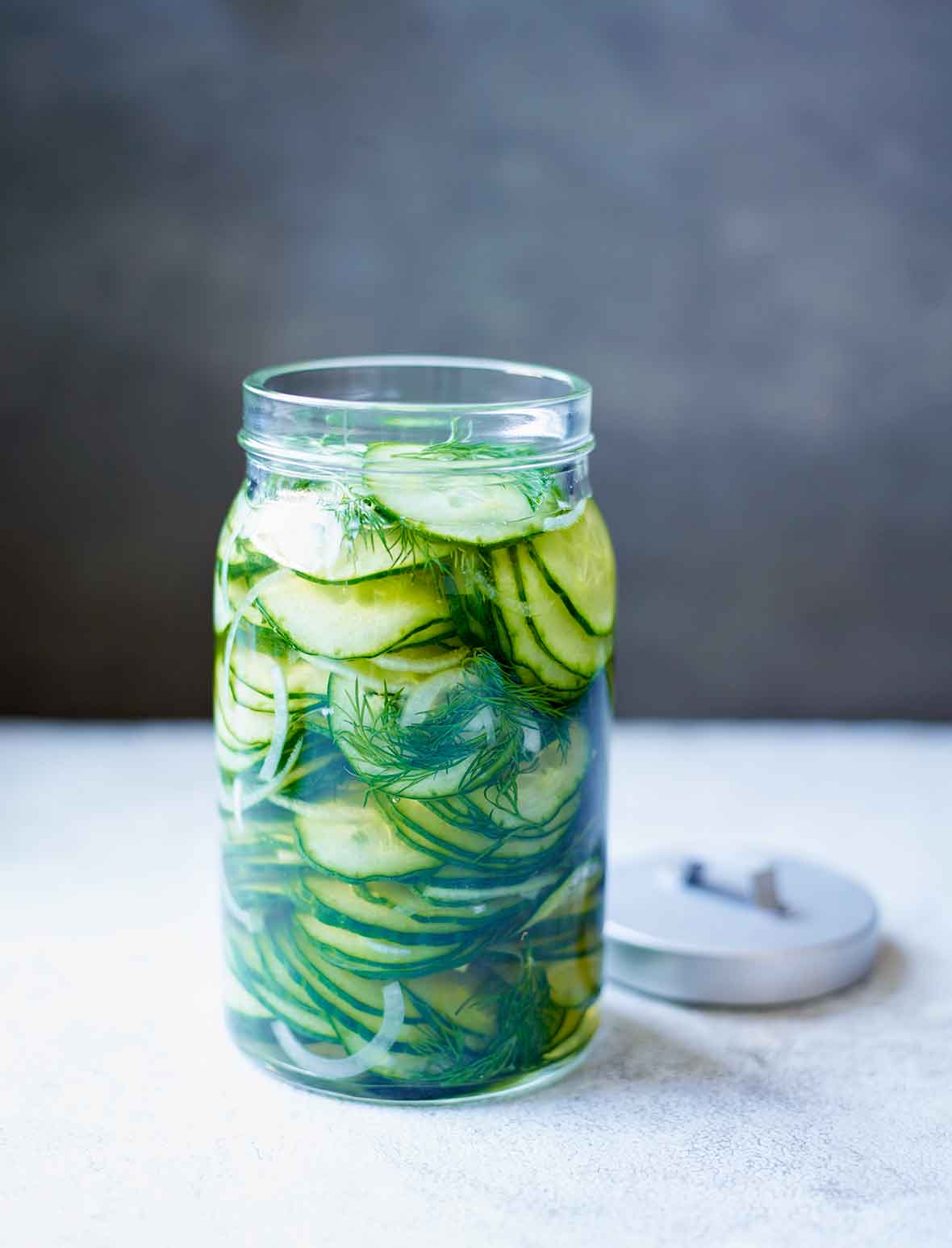 An open jar of refrigerator sweet pickles with the lid lying beside the jar.