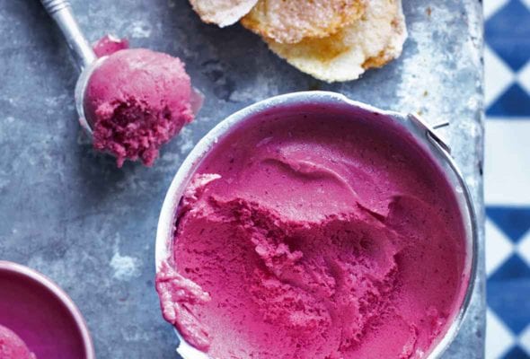 A bowl of plum sorbet with a metal ice cream scoop of plum sorbet beside it.