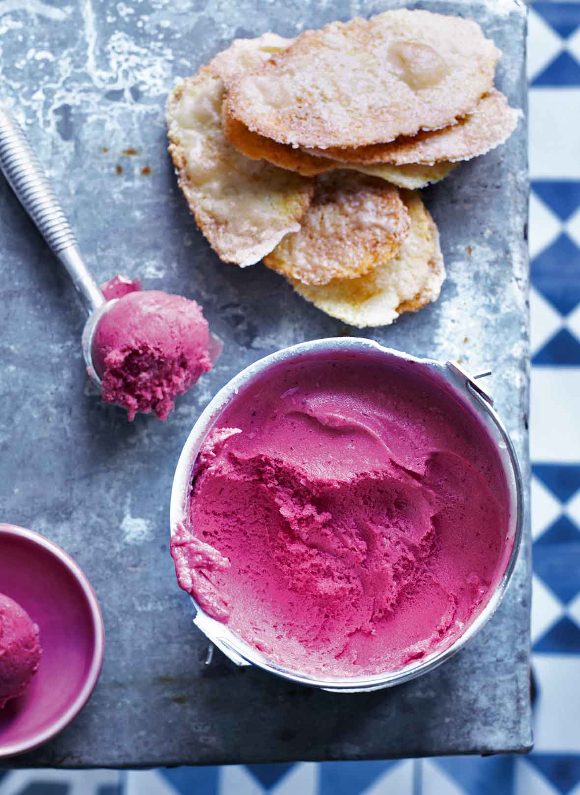 A bowl of plum sorbet with a metal ice cream scoop of plum sorbet beside it.