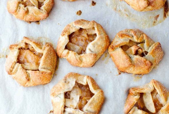 Seven rosemary apple hand tarts on a sheet of parchment.