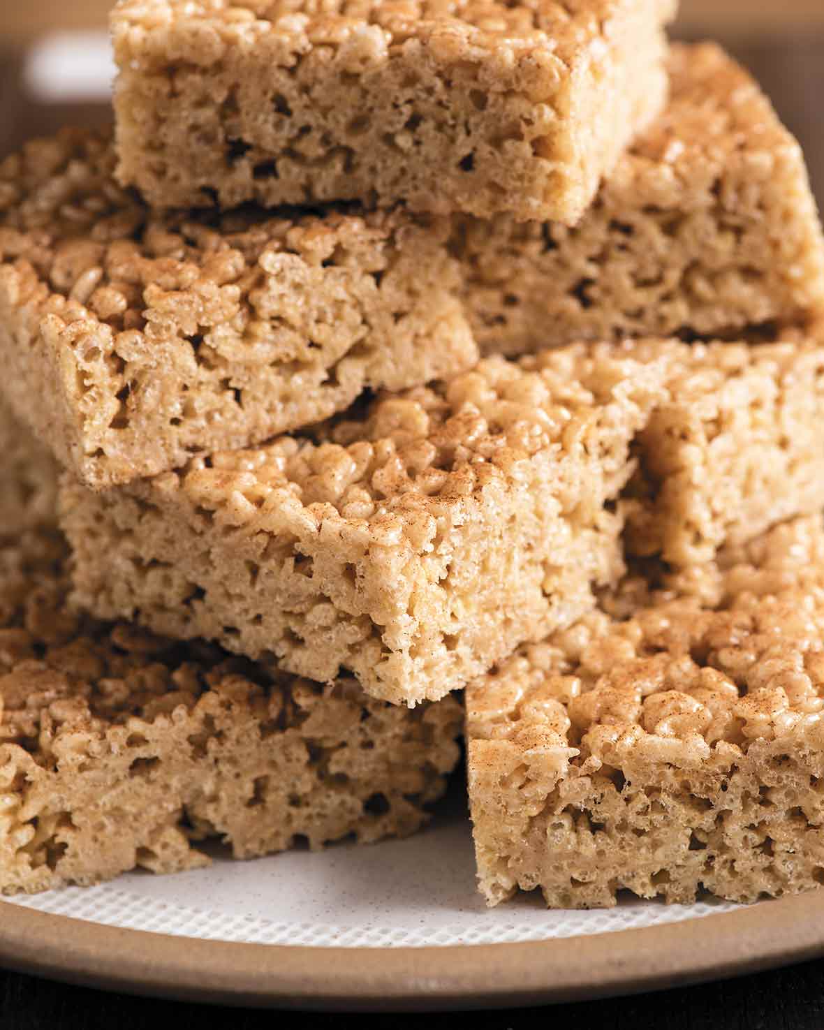 Several squares of pumpkin spice rice krispie treats stacked on a brown and white plate.