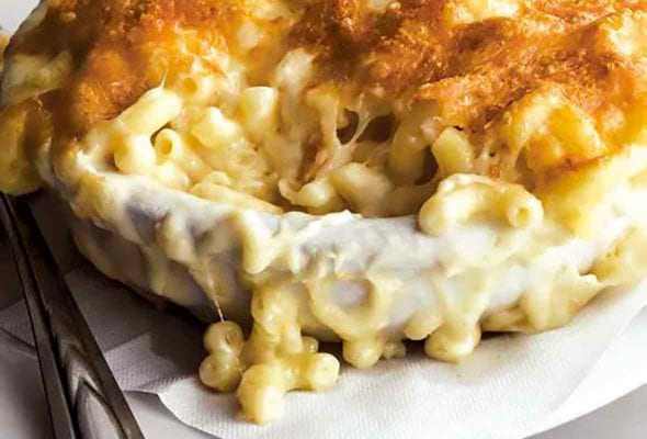 A dish of macaroni au gratin on a white paper napkin on a white plate with a stack of plates beside it.