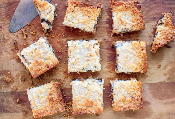 A slab of pumpkin seven layer bars cut into ten pieces on a wooden board.