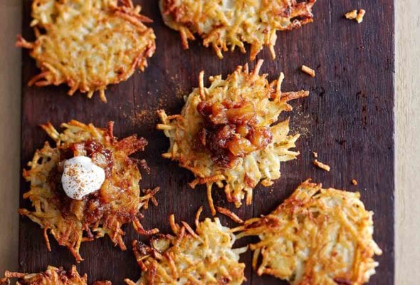 Nine potato latkes with apple-date chutney and cinnamon sour cream on a wooden cutting board.