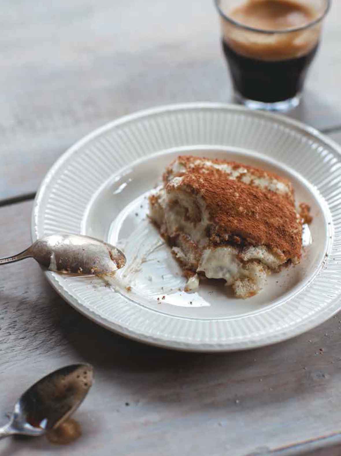 A piece of tiramisu in a white bowl with a spoon resting on the edge.