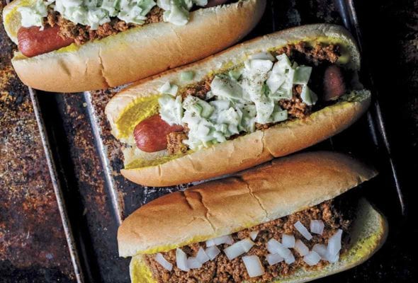 One chili bun and two slaw dogs on a rimmed baking sheet.