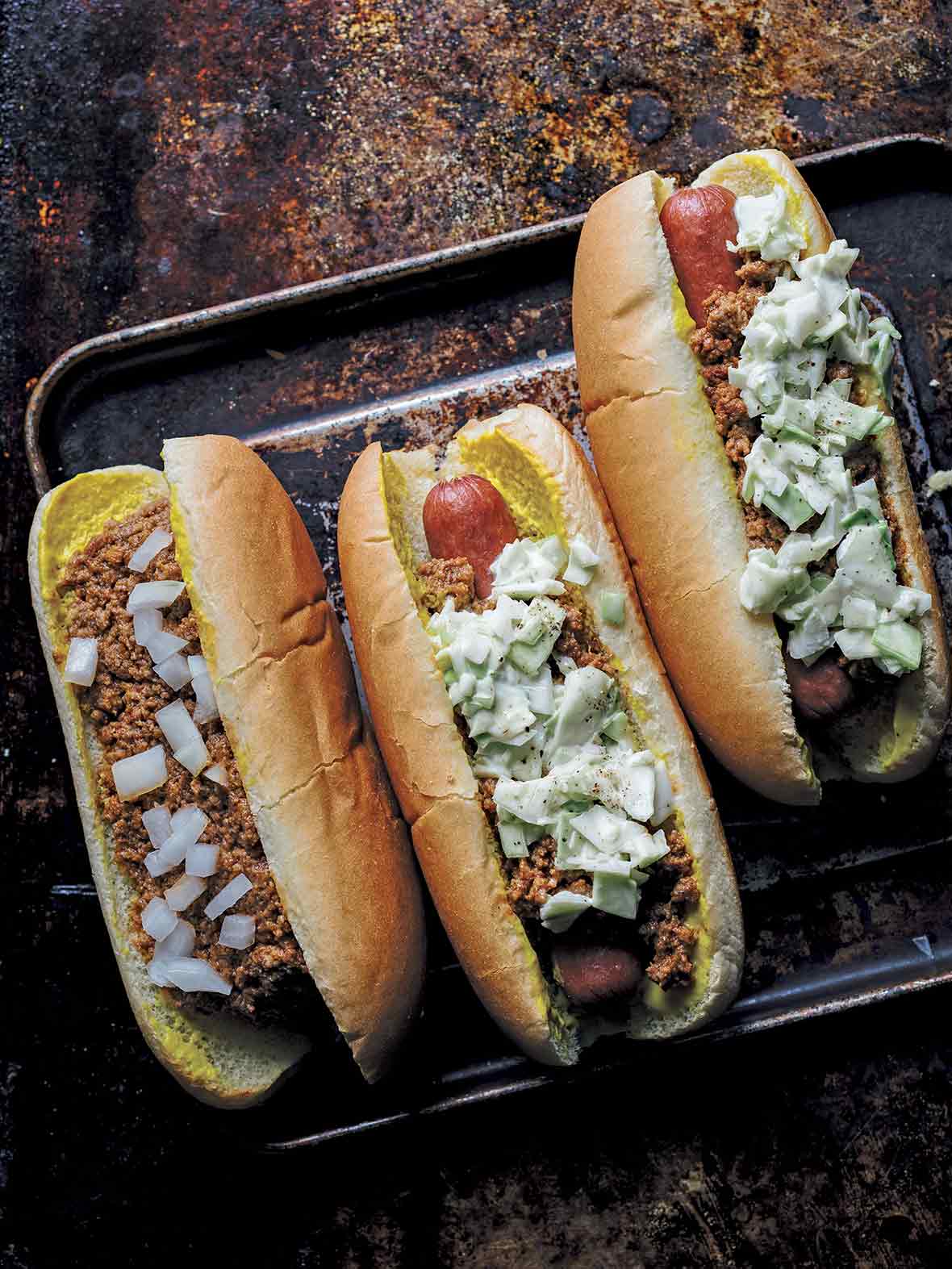 One chili bun and two slaw dogs on a rimmed baking sheet.