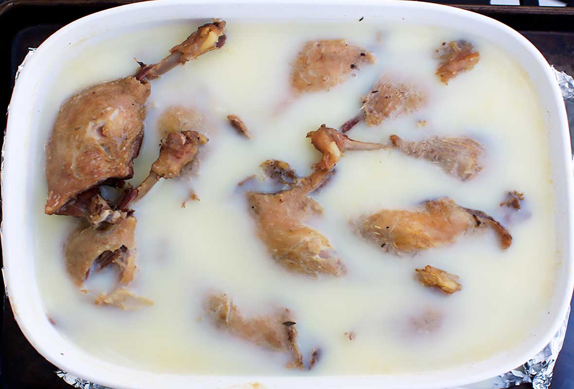 A white oval casserole dish filled with duck confit legs.