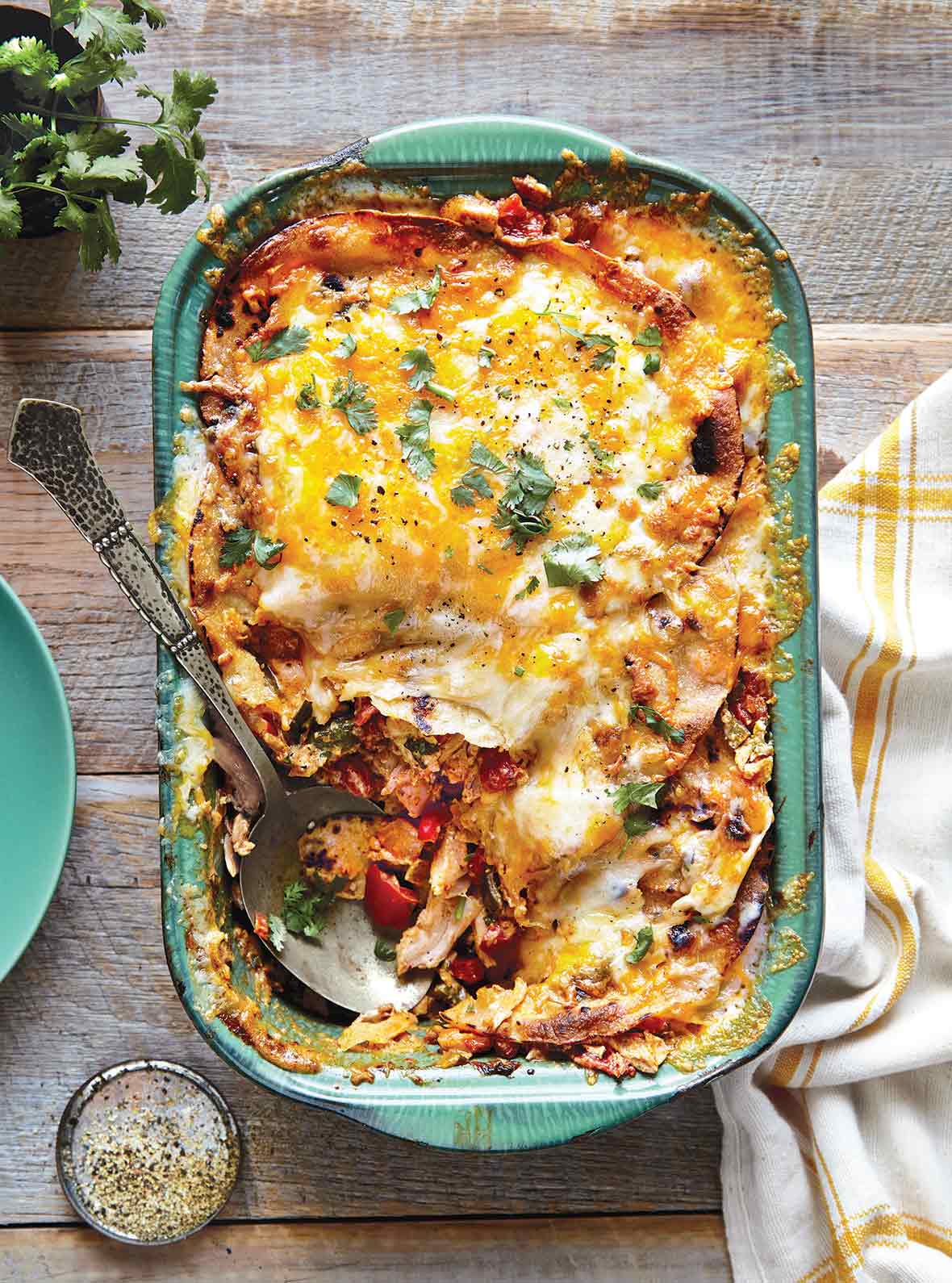 A green casserole dish filled with king ranch chicken casserole and a spoon resting in the dish.