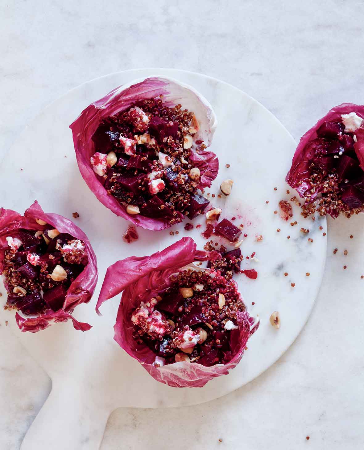 Four portions of roasted beet and quinoa salad served in a radicchio leaves on a white marble board.